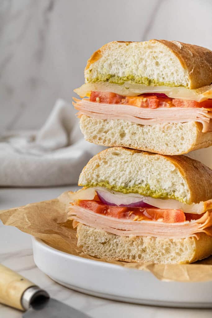 pieces of Costco Turkey and Provolone Sandwich stacked on each other on white plate with brown paper