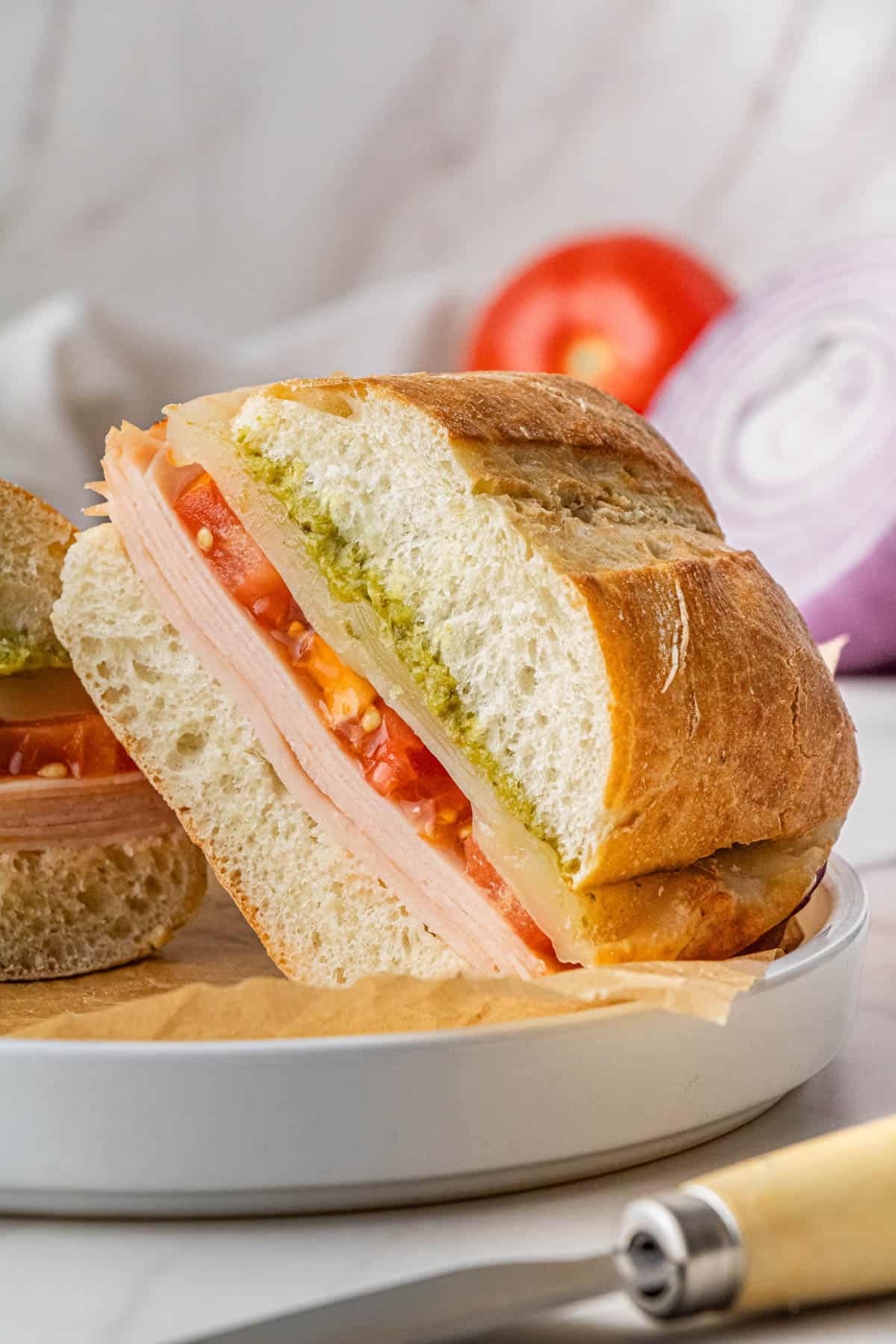 Costco Turkey and Provolone Sandwich stacked on each other on white plate with brown paper