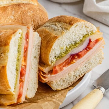 pieces of Costco Turkey and Provolone Sandwich stacked on each other on white plate with brown paper