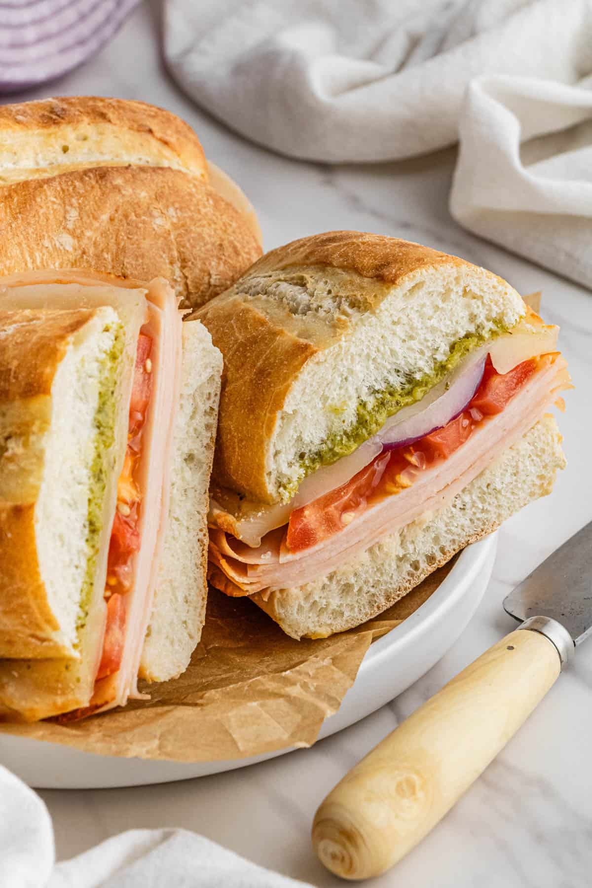 pieces of Costco Turkey and Provolone Sandwich stacked on each other on white plate with brown paper