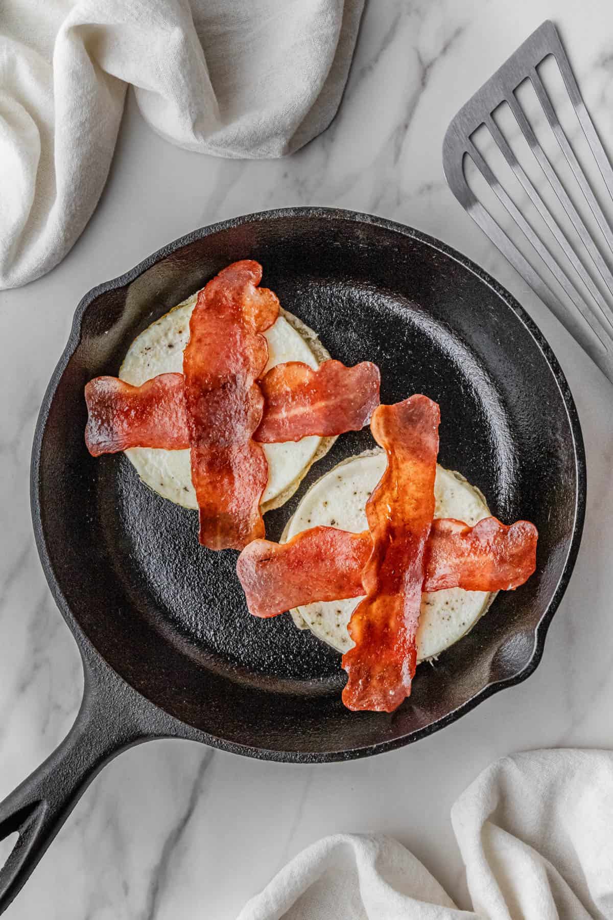 two pieces of meat on egg white and English muffin in skillet