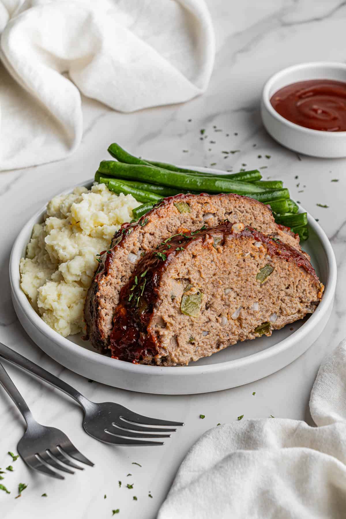 slices of Cracker Barrel Meatloaf recipe on a white plate with mashed potatoes and green beans