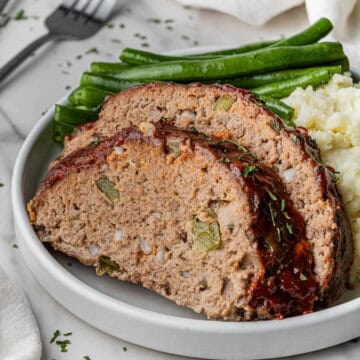 slices of Cracker Barrel Meatloaf recipe on a white plate with mashed potatoes and green beans