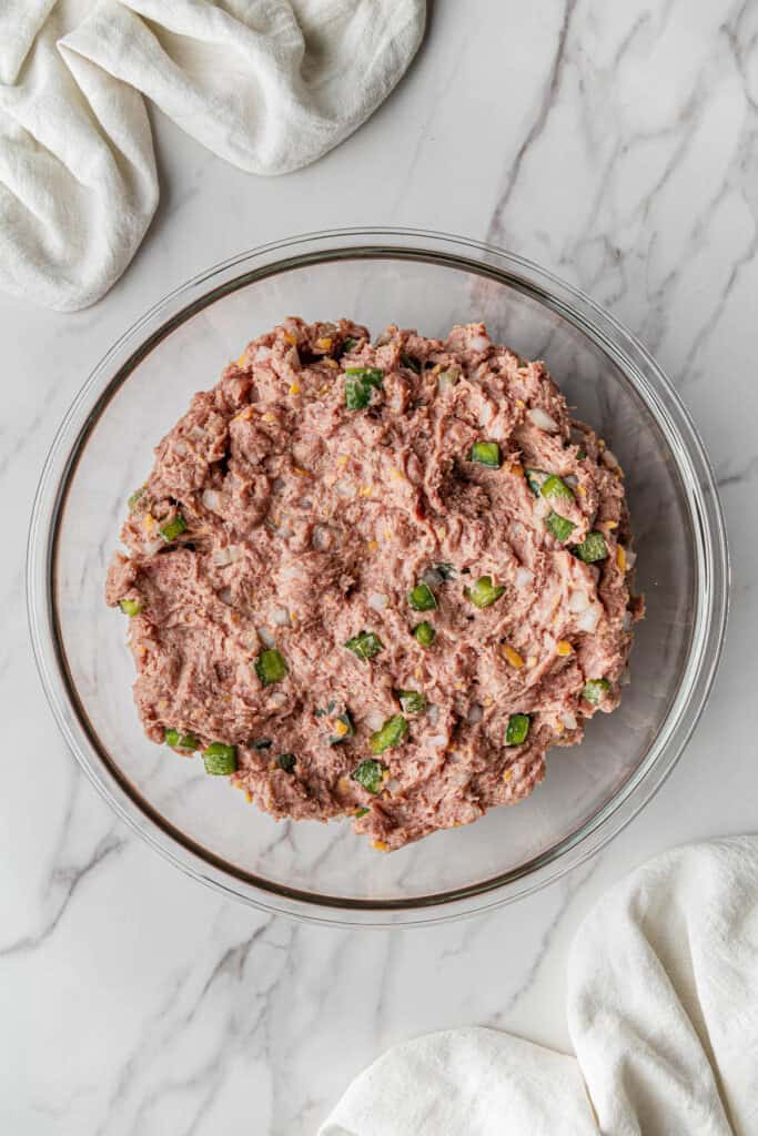 ingredient mixture with green peppers in clear mixing bowl