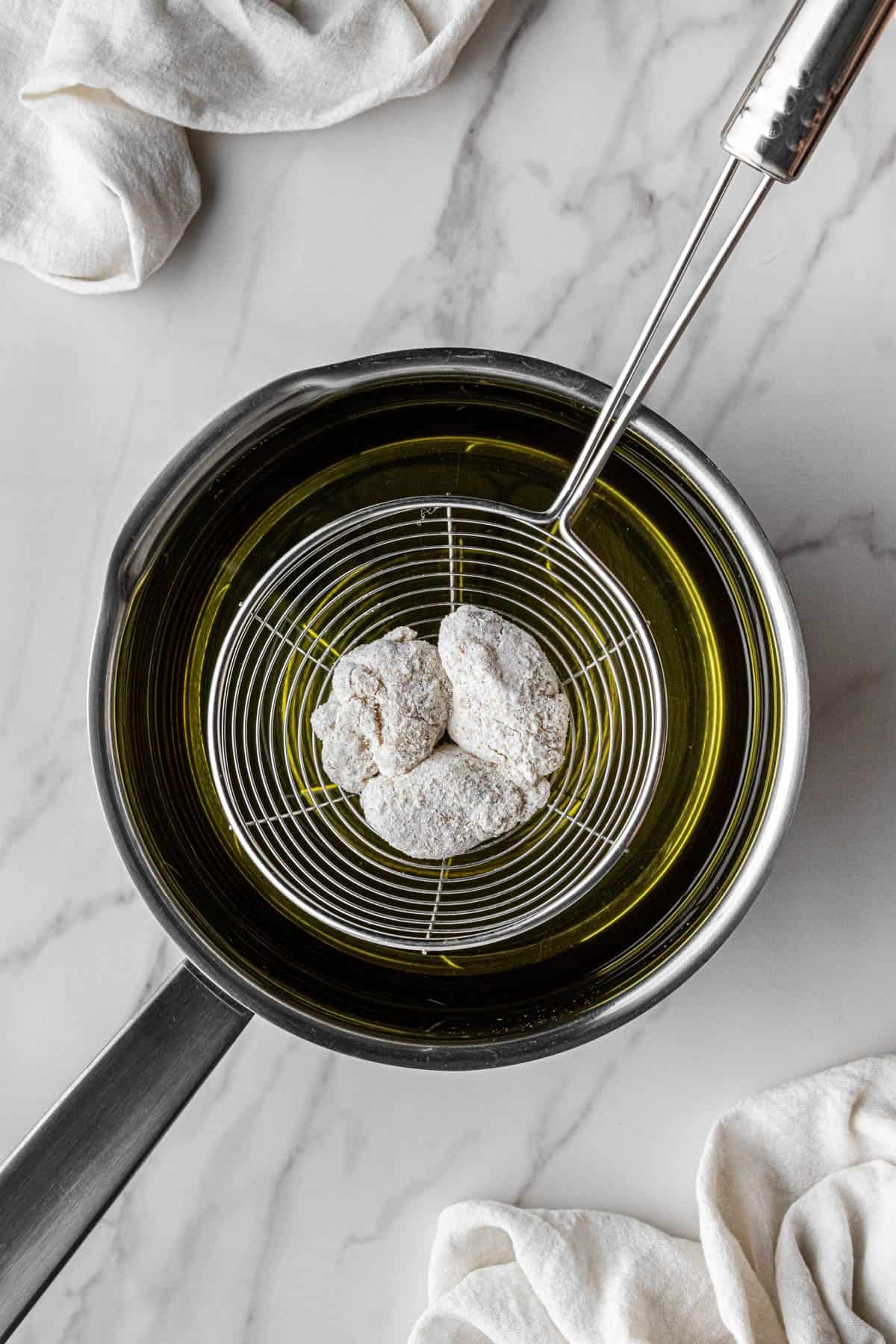 breading coated raw meat above pot of hot oil in strainer