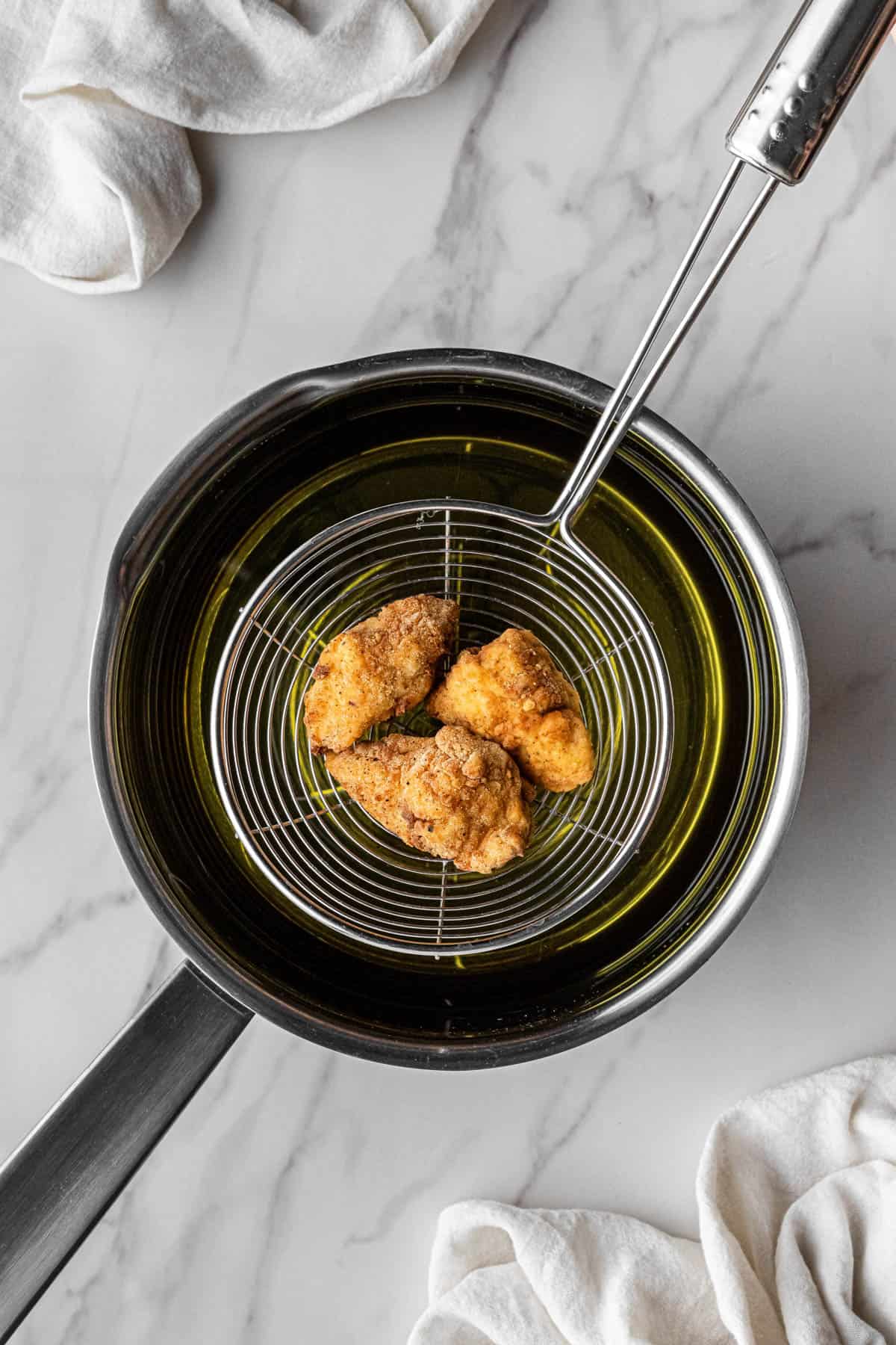 cooked meat pieces over frying oil in strainer