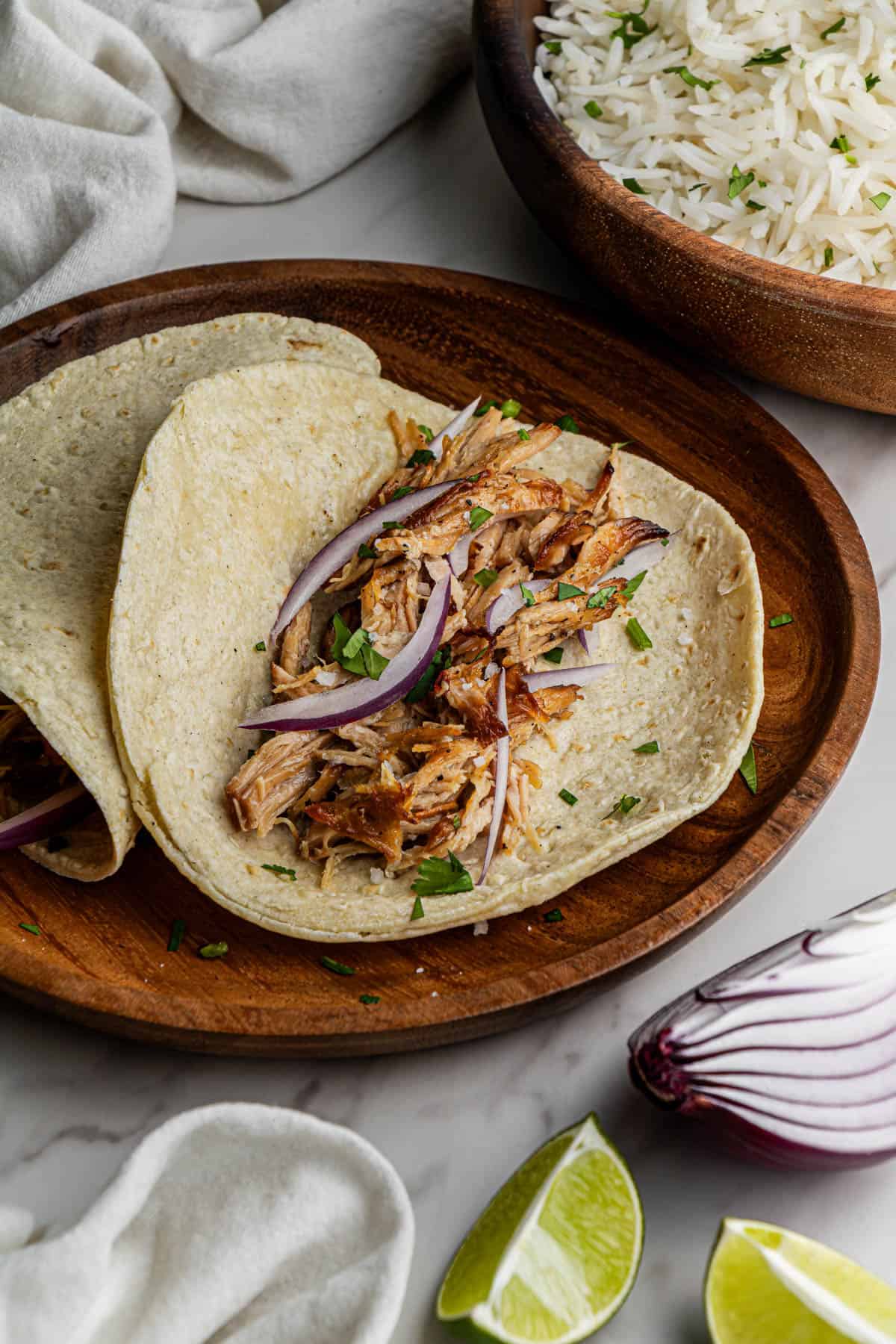 Two tacos filled with the Copycat Chipotle Carnitas. The tacos are served on a wooden plate.