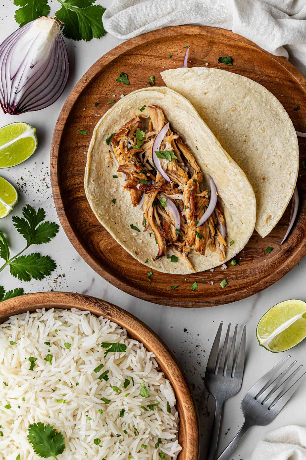 Flat lay shot of the tacos with the Chipotle Carnitas Copycat recipe on the flour tortilla. Beside the wooden plate is a wooden bowl with cilantro rice.