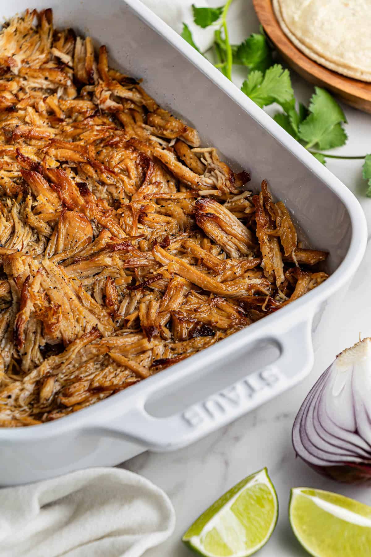 Partial shot of a white baking dish with the finished shredded Chipotle Carnitas Copycat Recipe.