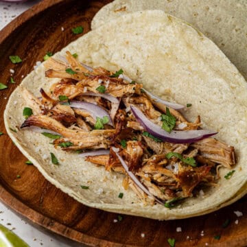 A taco with the Chipotle Carnitas Copycat Recipe in it. The taco is on a wooden plate on a marble surface.