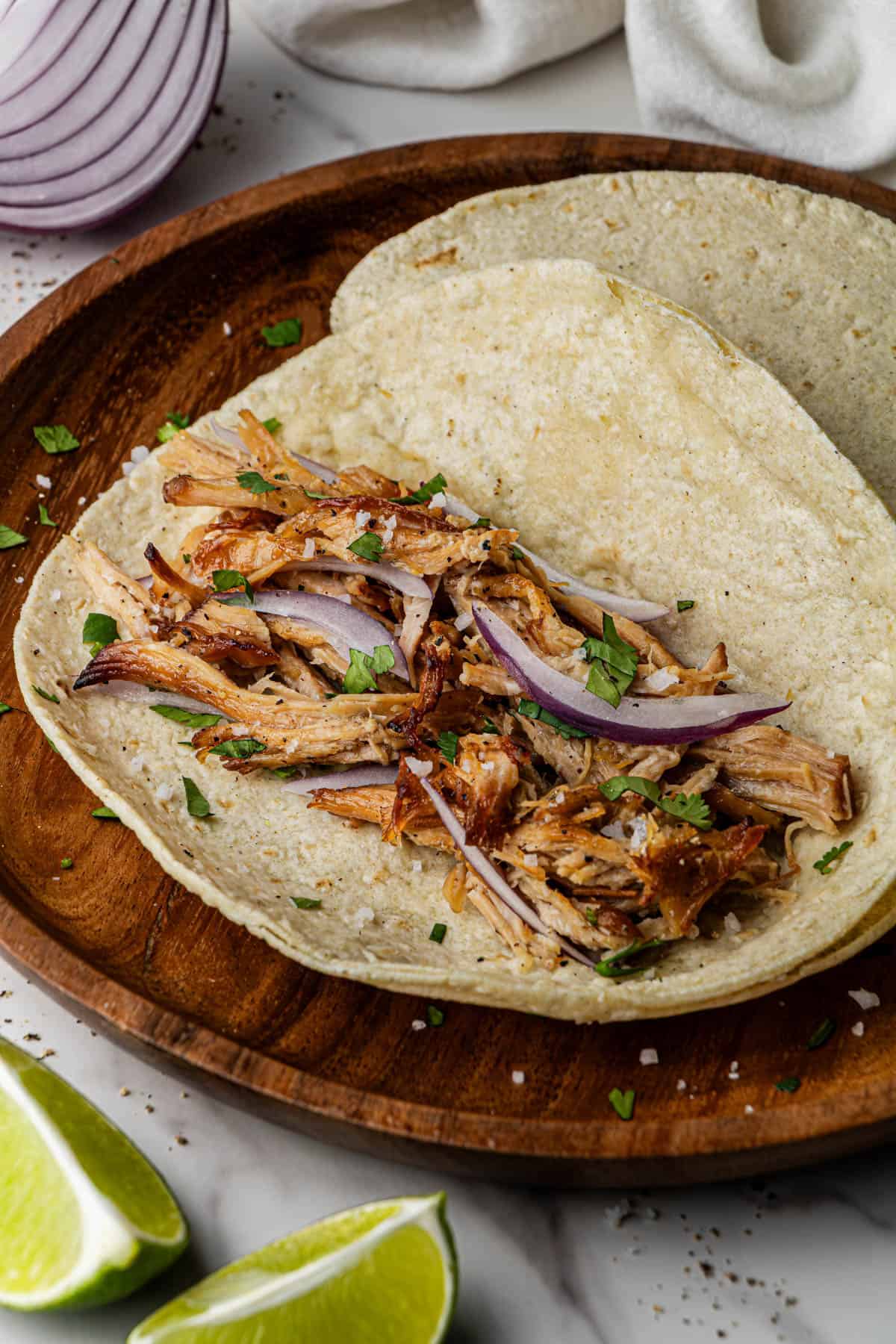 A taco with the Chipotle Carnitas Copycat Recipe in it. The taco is on a wooden plate on a marble surface.