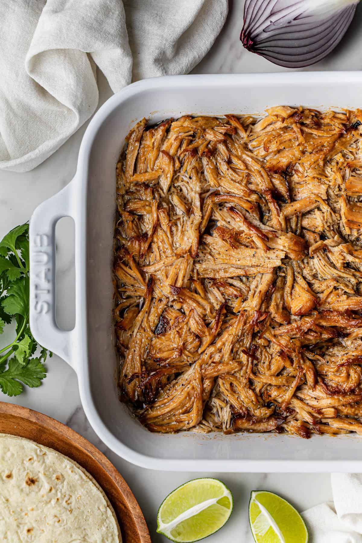 Flat lay, partial shot of a white baking dish with the finished Chipotle Carnitas Copycat Recipe.