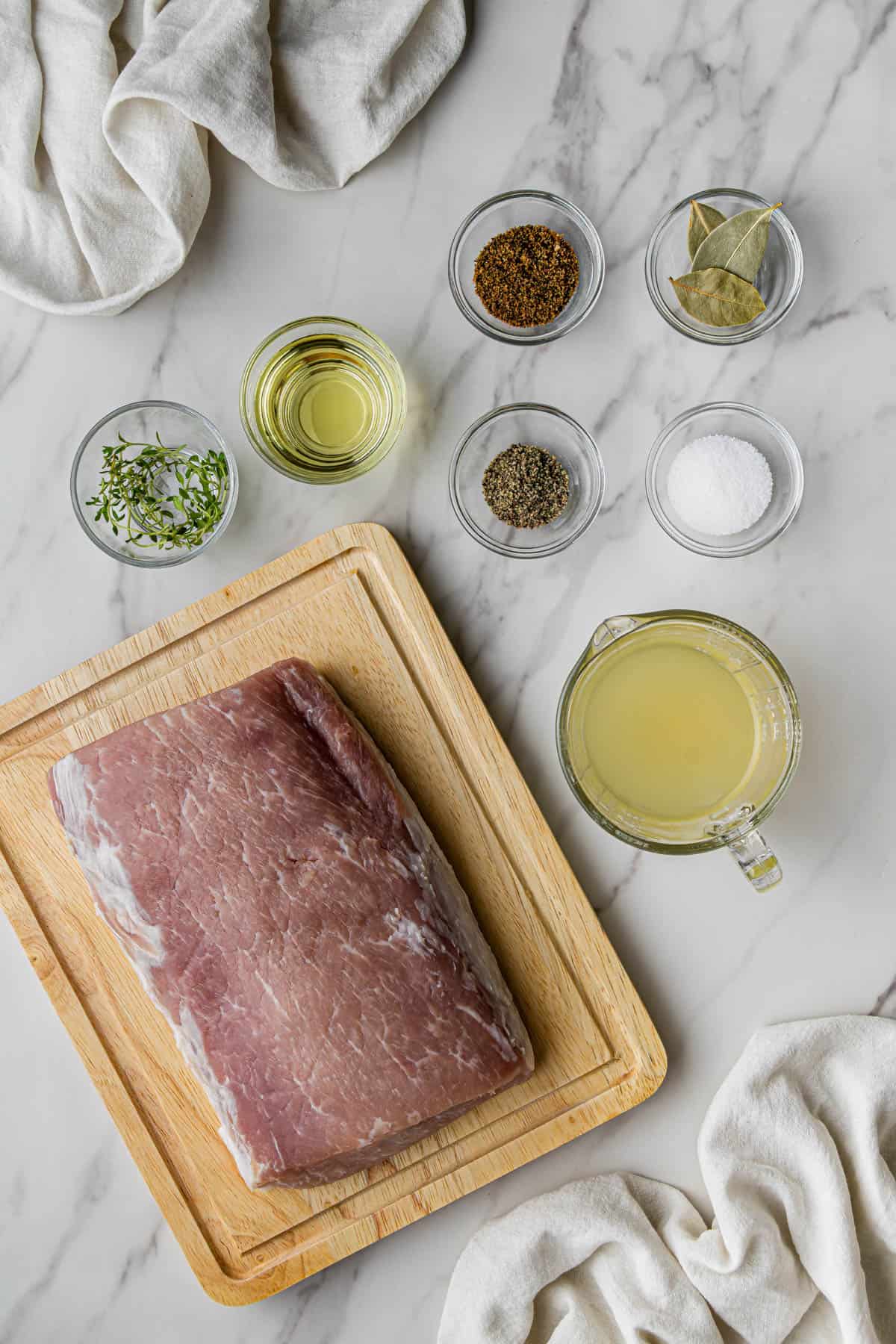 Flat lay shot of the ingredients for the Chipotle Carnitas Copycat Recipe, all placed in separate glass bowls and on a marble surface.