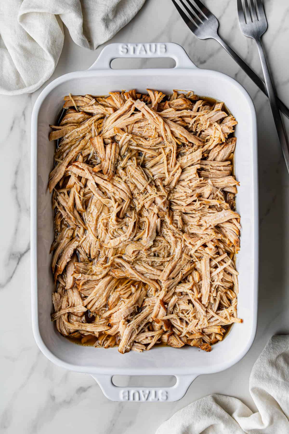 Flat lay shot of a white baking dish with shredded meat in it.