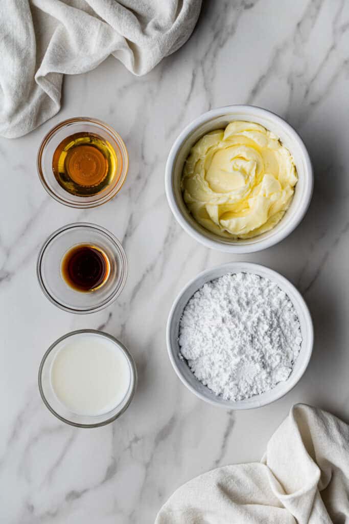 Flat lay shot of the ingredients for the honey buttercream. The ingredients are placed on separate bowls and arranged neatly on a marble surface.