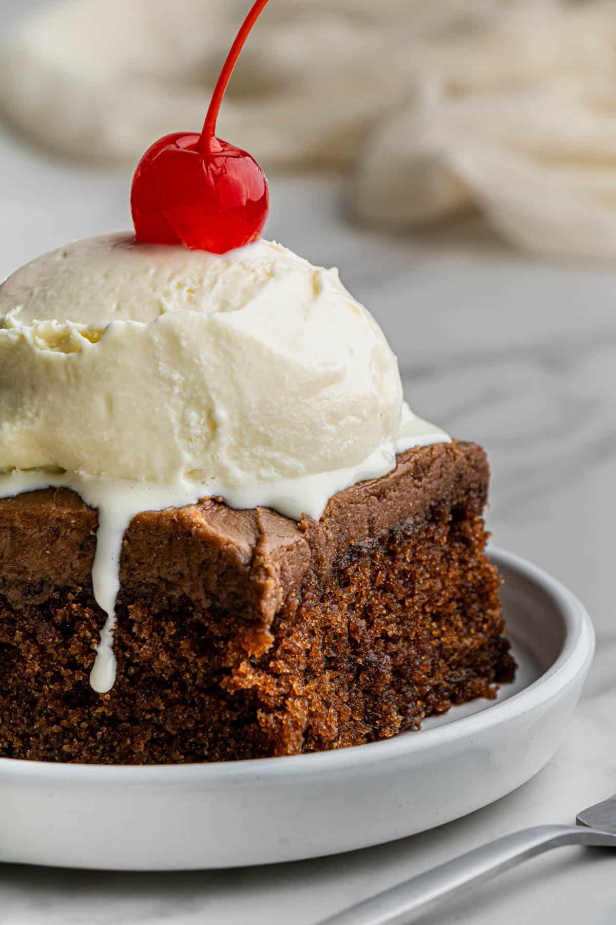 Closeup shot of a slice of the finished cracker barrel Coca cola cake recipe with a scoop of vanilla ice cream and cherry on top.