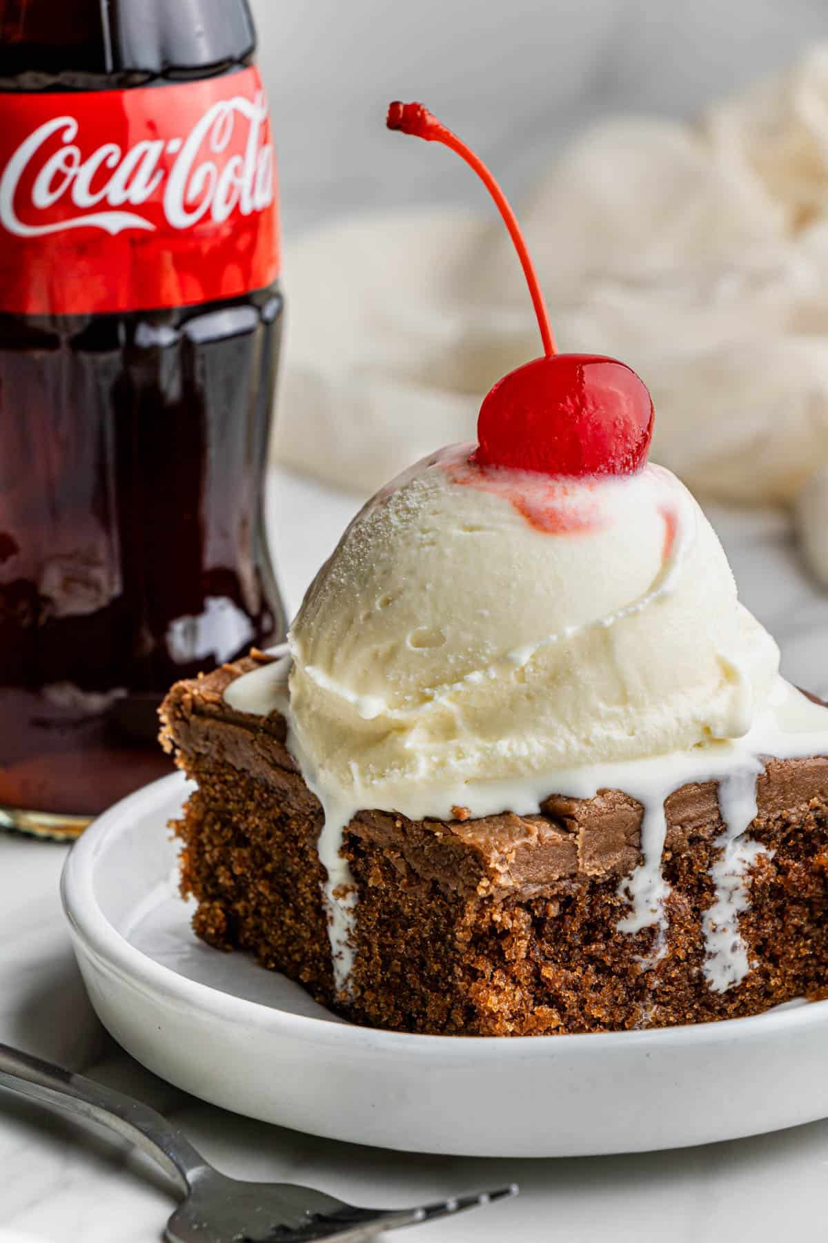 A slice of the cracker barrel Coca-Cola Cake recipe with a scoop of vanilla ice cream with a cherry on top.