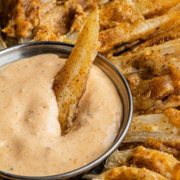 A single onion petal dipped into the signature outback Bloomin' Onion sauce copycat recipe in a small bowl in the middle of the entire fried whole onion.