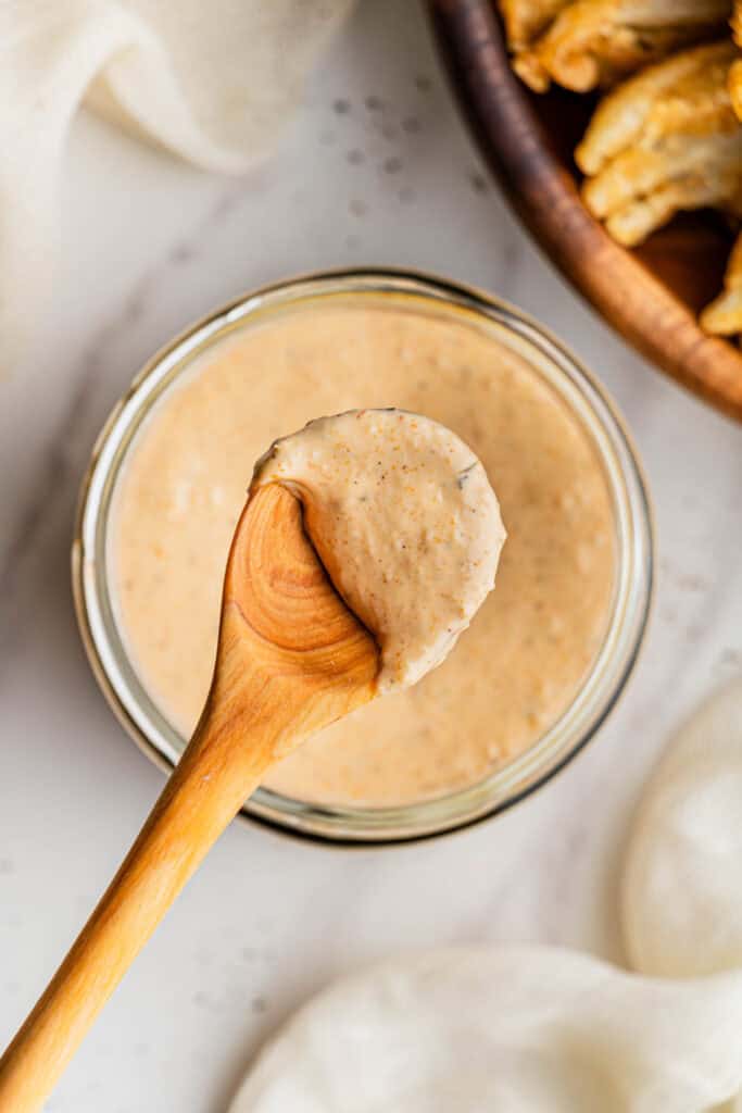Flat lay shot of a wooden spoon that was dipped on some sauce in a jar beneath it.