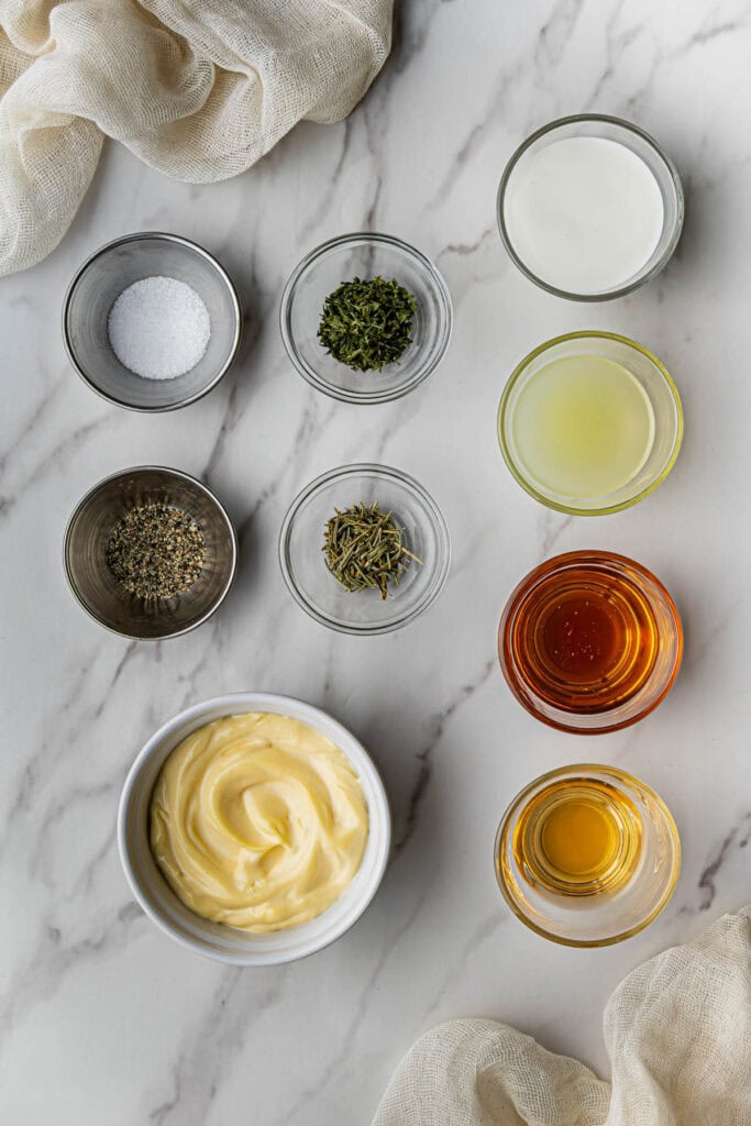 Flat lay shot of condiments, spices, and herbs for the chicken salad. The ingredients are in separate bowls and placed on a marble surface.