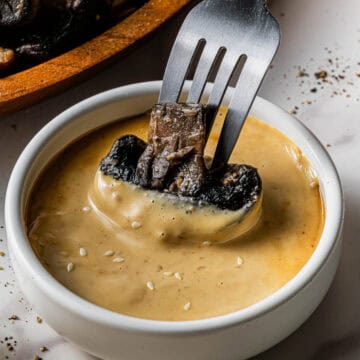 A cooked broccoli being dipped into a small white bowl with Benihana Copycat Mustard Sauce recipe in it.