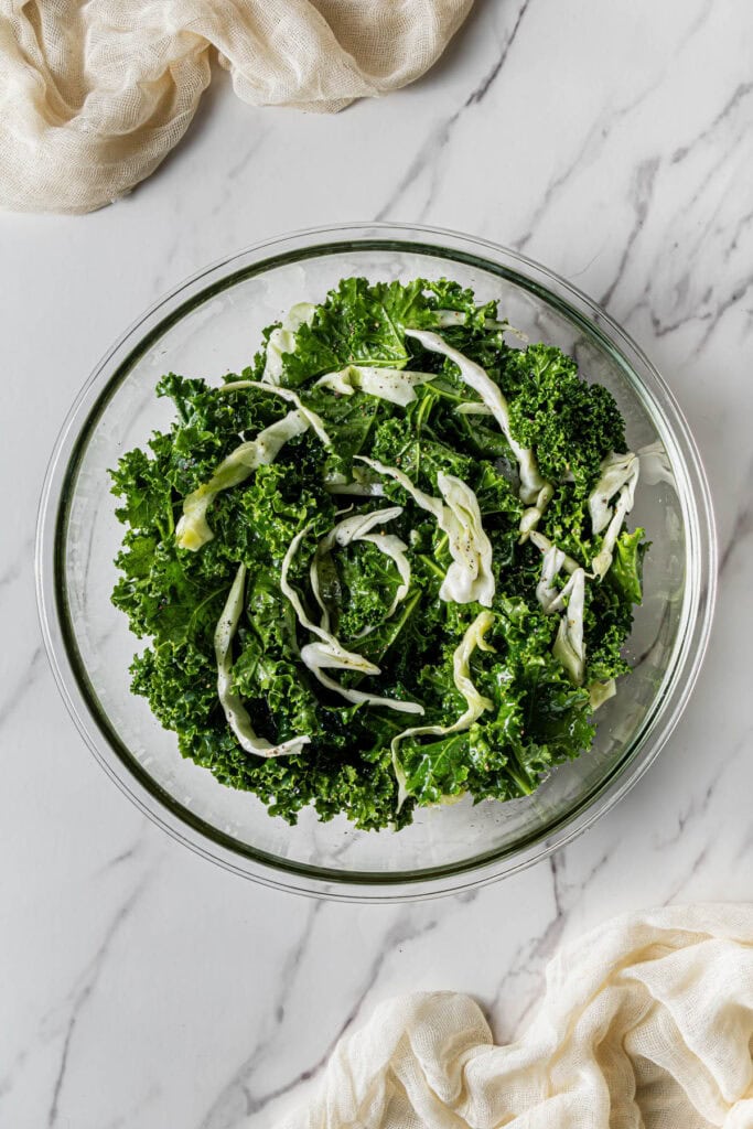 A glass bowl with greens and shredded cabbage in it.
