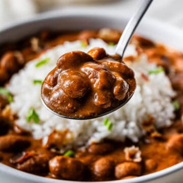 Focus shot of a spoonful of Popeye's Copycat Red Beans and Rice. Behind it is a dish filled with more Red Beans and Rice.