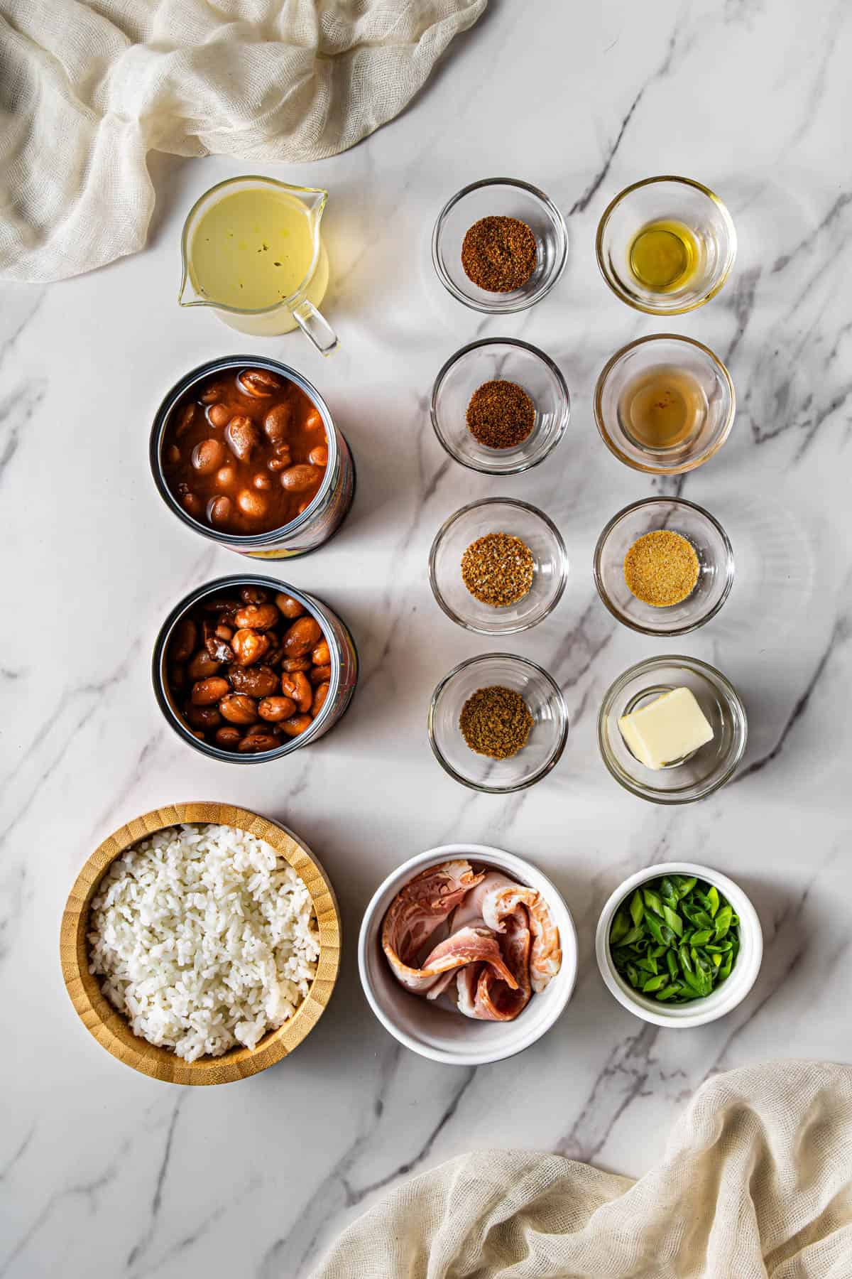 Flat lay shot of the ingredients to make Red Beans and Rice. Each ingredient is on its own bowl, then placed on a marble surface.