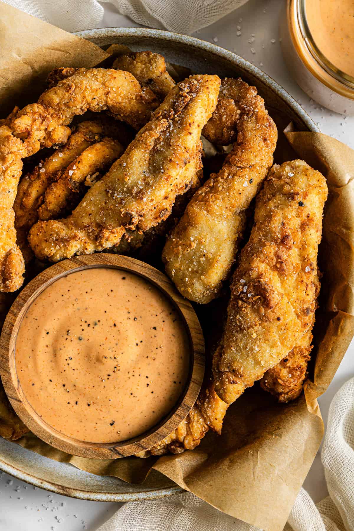 Bowl filled with crispy chicken tenders and a small wooden bowl of creamy dipping sauce.