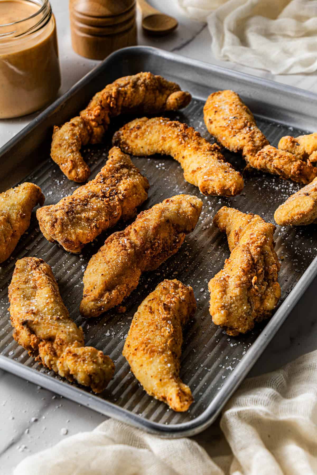 Golden crispy chicken tenders arranged on a baking tray and sprinkled with flaky salt.