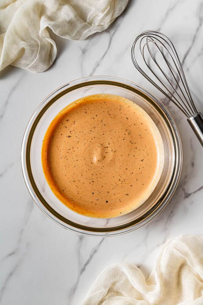 Glass bowl filled with a smooth, seasoned dipping sauce with black pepper specks throughout.