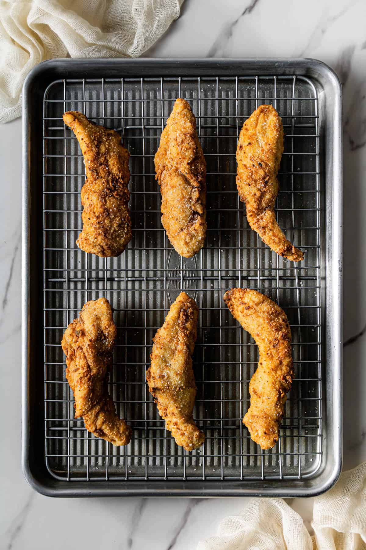 Golden crispy fried chicken tenders cooling on a wire rack.