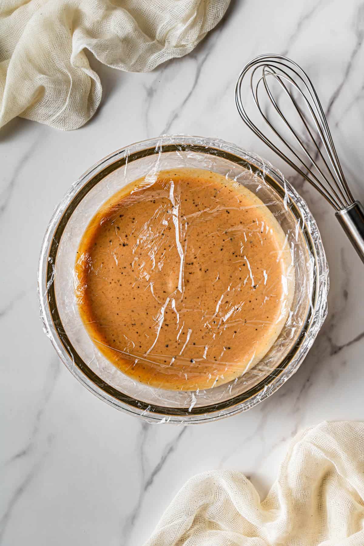 A glass bowl with the Raising Cane sauce that's covered with plastic wrap.