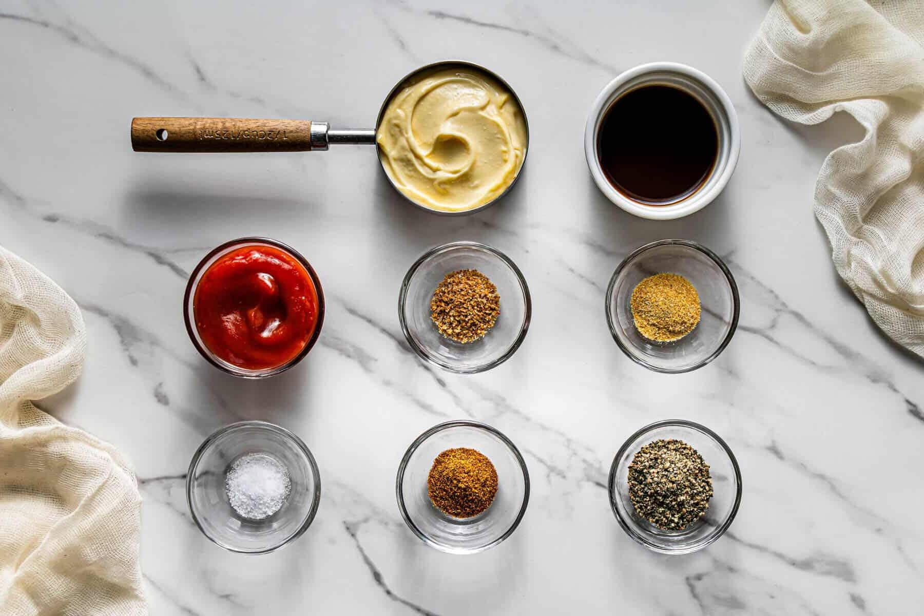 Flat lay shot of the ingredients to make the Raising Cane sauce. Each ingredient is on a glass bowl, placed on a marble surface.