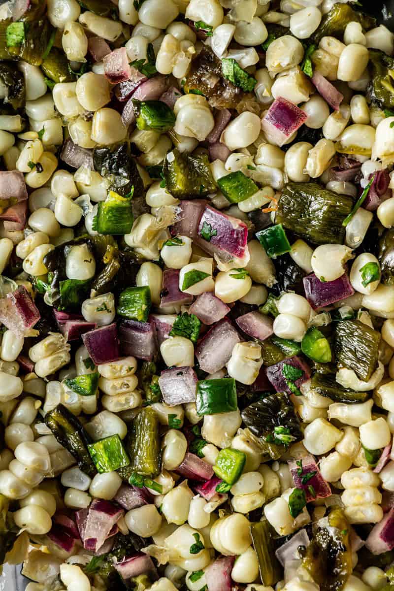 Close-up of white corn kernels, roasted poblano, jalapeño, and red onion in corn salsa