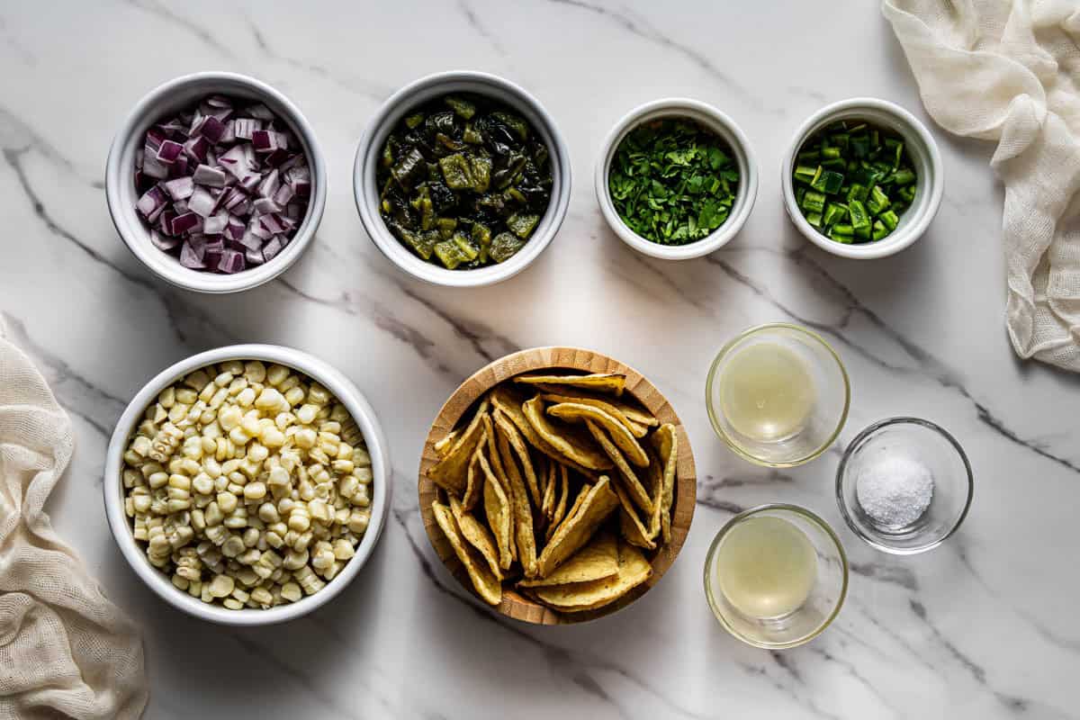 Chipotle corn salsa ingredients laid out in bowls on a marble surface