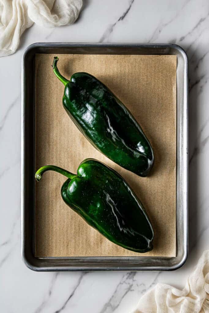 Two raw poblano peppers on a parchment-lined baking sheet