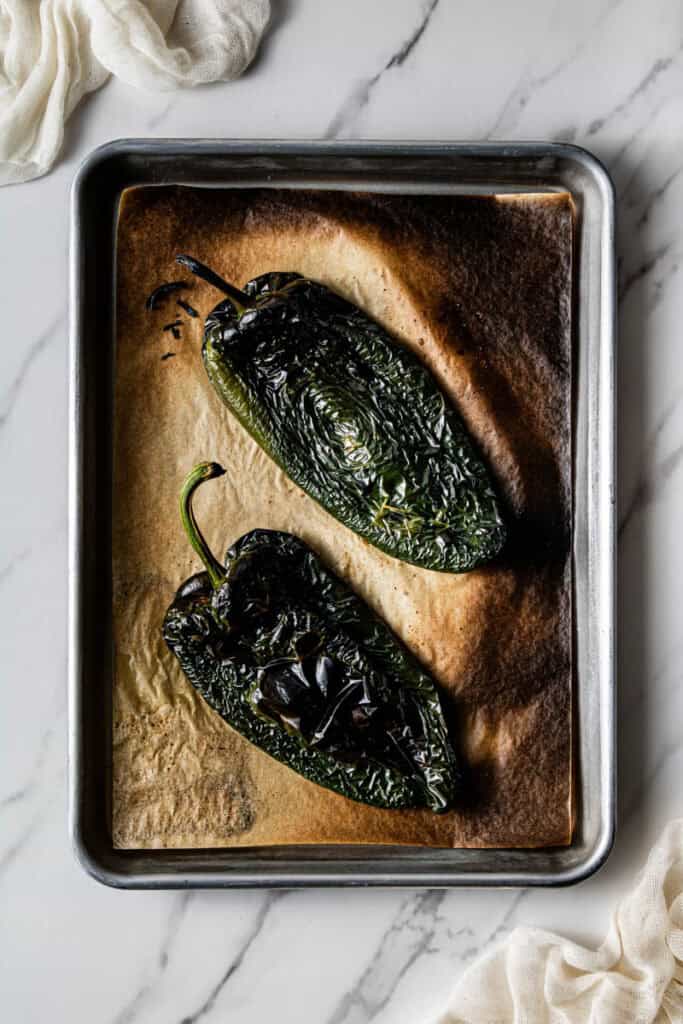 Two charred roasted poblano peppers on a baking sheet