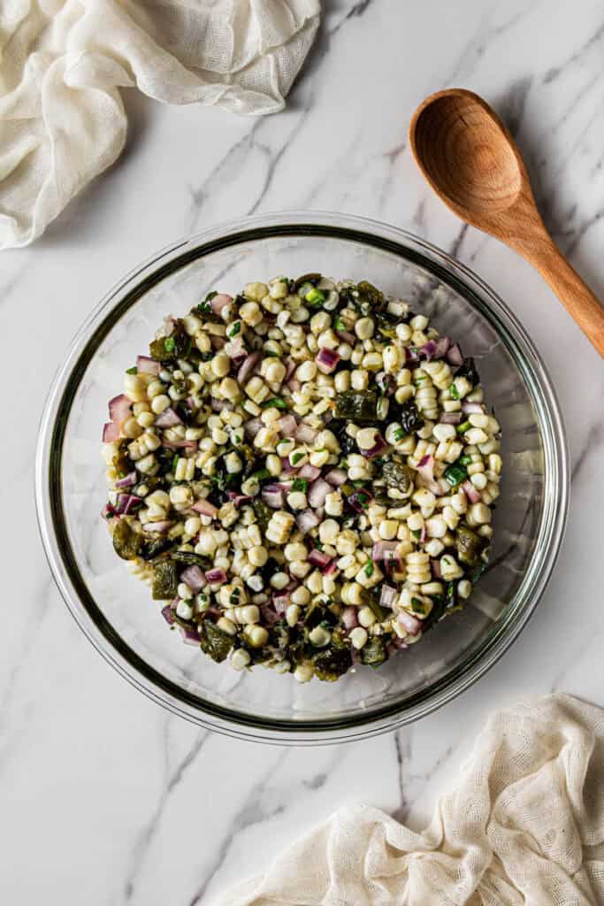 White corn kernels folded into the salsa mixture in a glass bowl