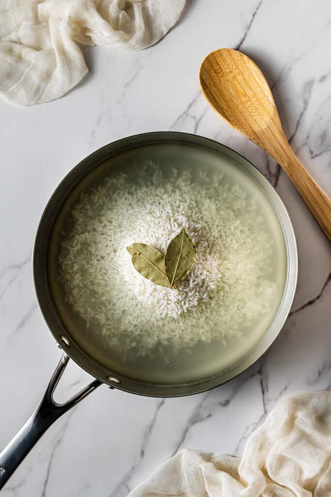 Long-grain rice cooking in chicken broth with bay leaves for Popeye’s dirty rice