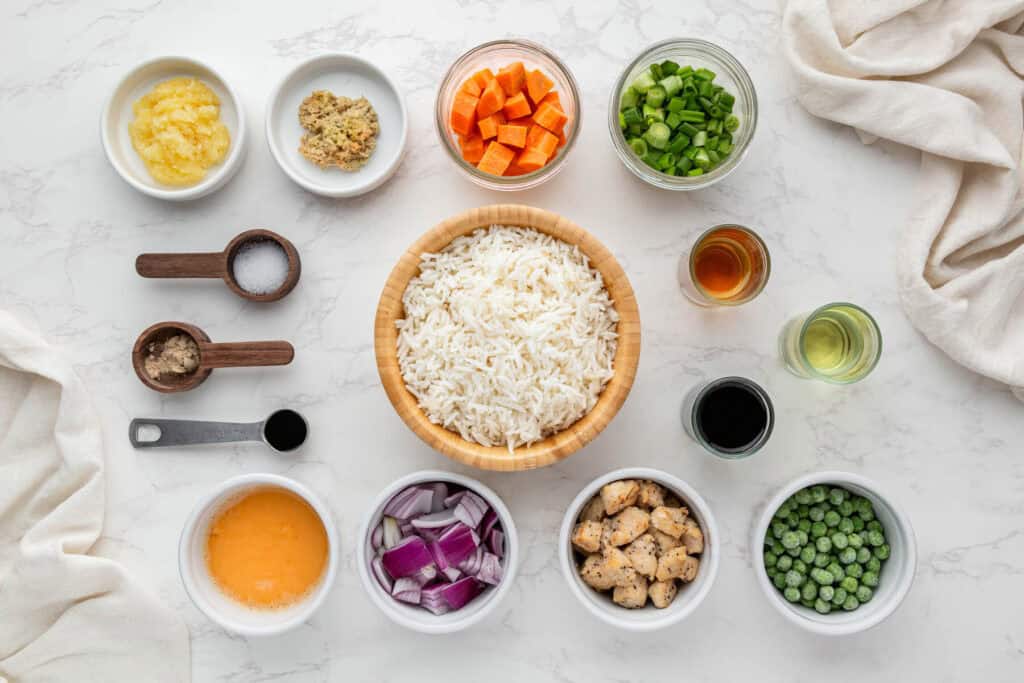 Ingredients for chicken fried rice including jasmine rice, chicken breast, eggs, peas, carrots, soy sauce, sesame oil, garlic, and ginger