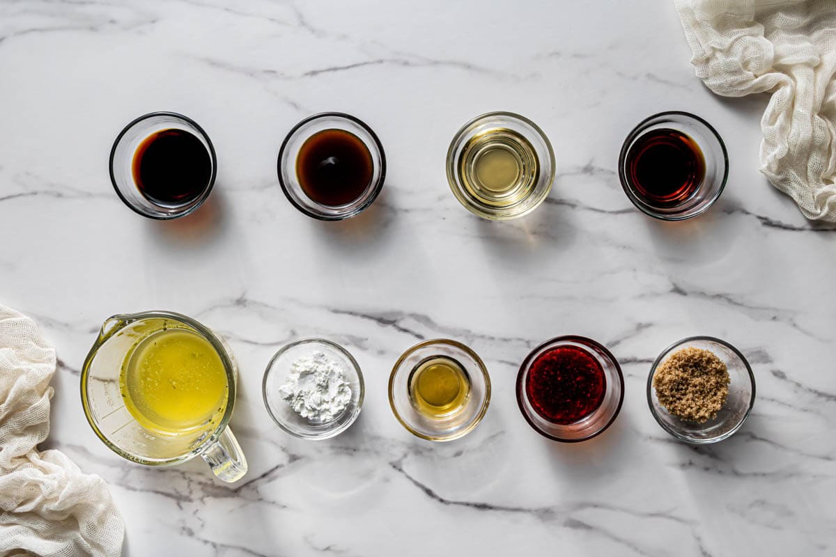 Kung pao sauce ingredients in small glass bowls including soy sauce, dark soy sauce, oyster sauce, rice vinegar, sesame oil, chili crisp, cornstarch, and brown sugar on marble