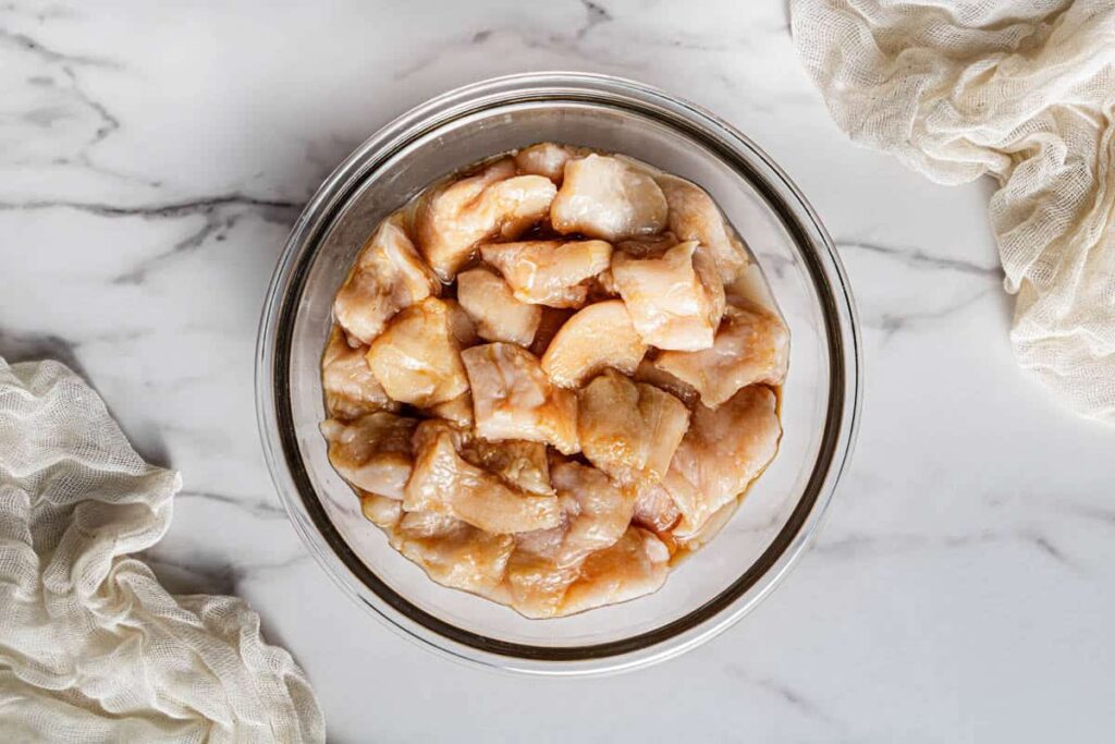 Chicken thigh pieces coated in marinade in a glass mixing bowl