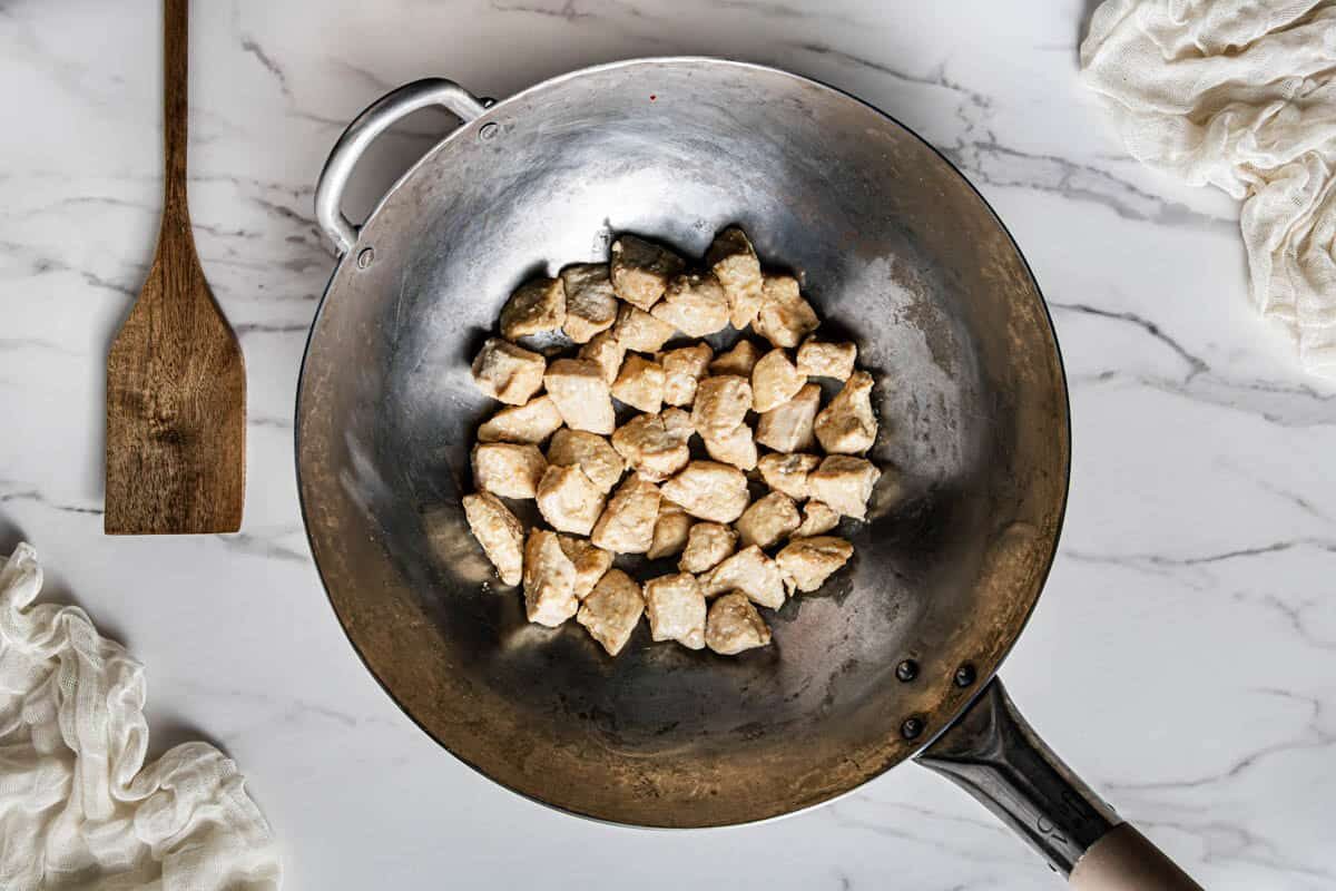 Cooked chicken thigh pieces seared in a carbon steel wok with a wooden spatula