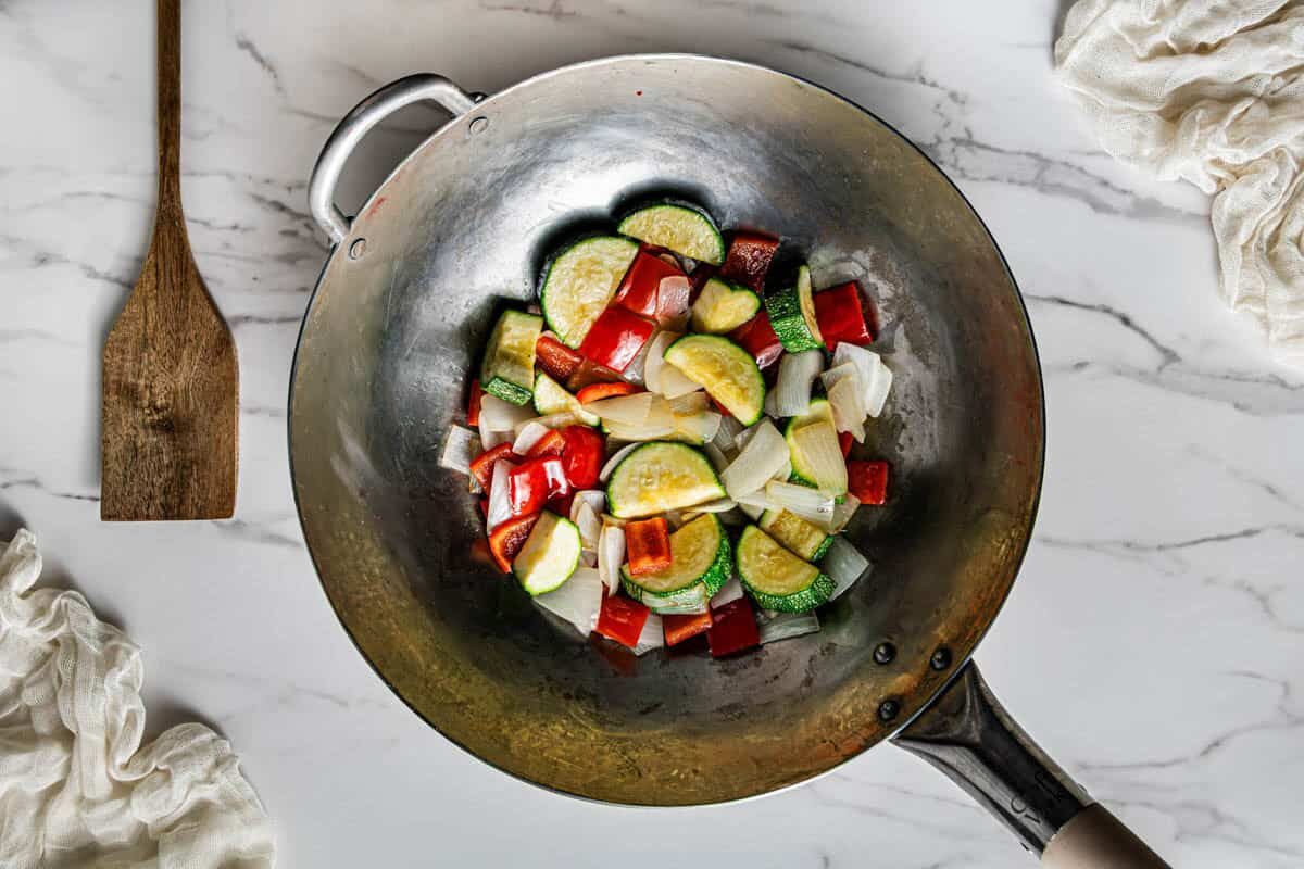Zucchini, red bell pepper, and onion stir frying in a carbon steel wok
