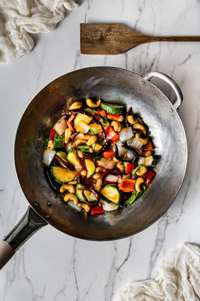 Kung pao sauce coating stir-fried zucchini, red bell pepper, onion, cashews, and dried chilies in a carbon steel wok