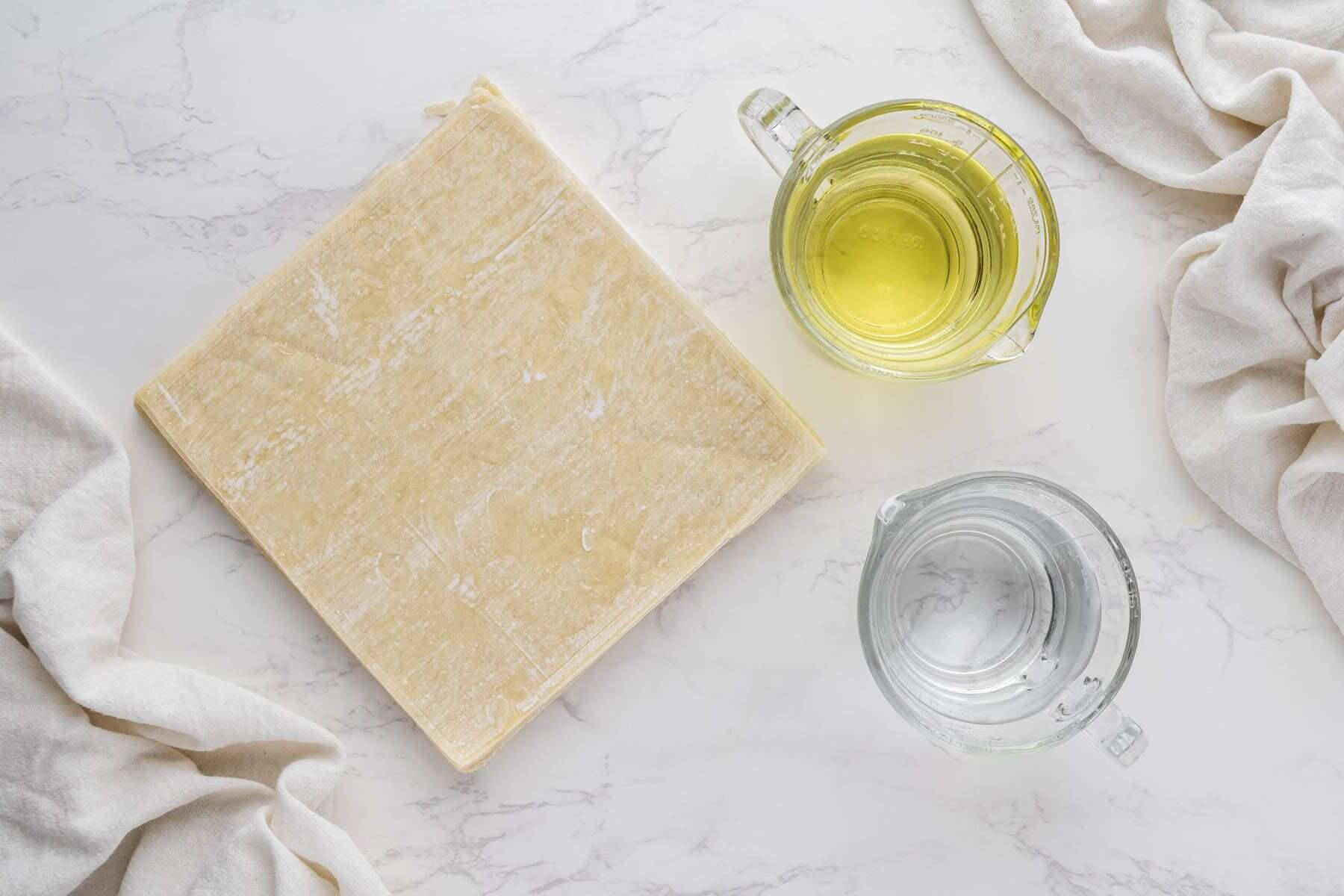 overhead view of egg roll wrappers, water and oil in individual cups